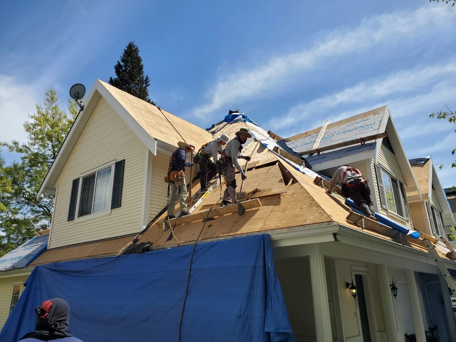 Roofers working on a house roof under a blue sky, some wearing safety gear.