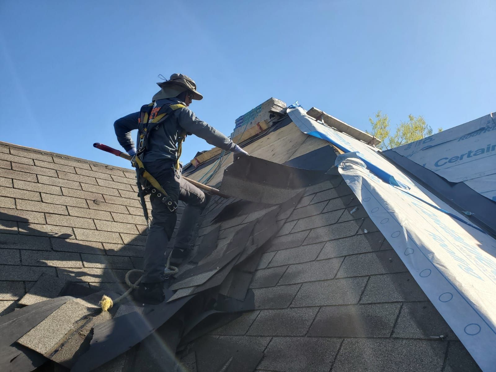 Roofing worker installing shingles on a steep roof under a blue sky