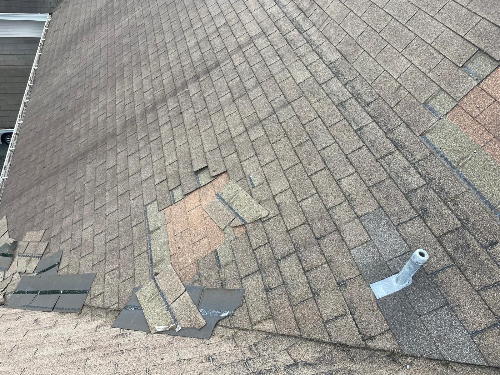 Damaged asphalt shingle roof, shingles missing or displaced, some areas discolored.