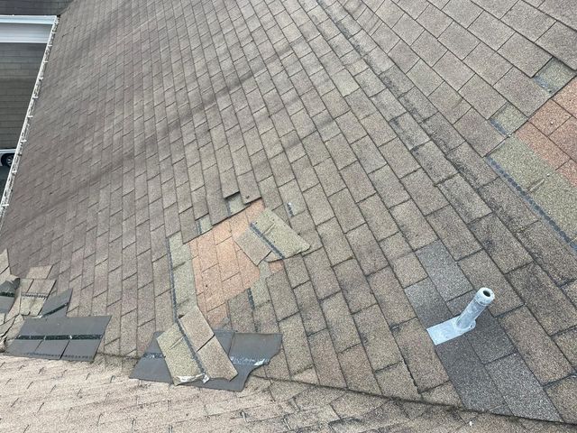 Shingle roof surface with lifted roofing pieces and a metal pipe flashing