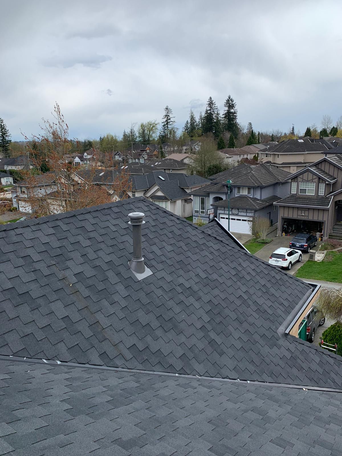 A view from a residential roof looking out over a suburban neighborhood with houses, trees, and a street below.