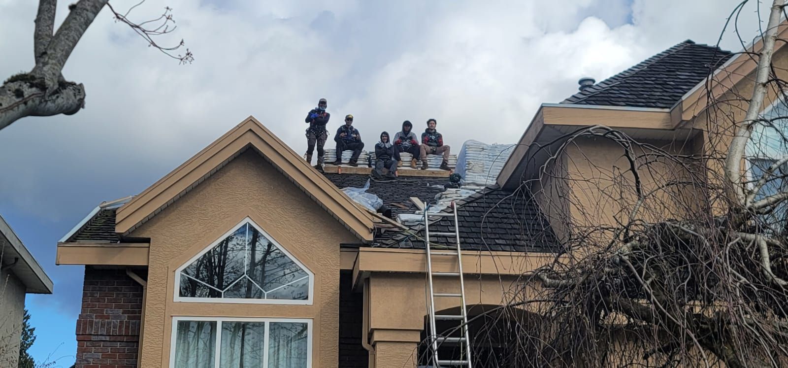 Five workers sit on scaffolding on the roof of a beige residential house during construction.