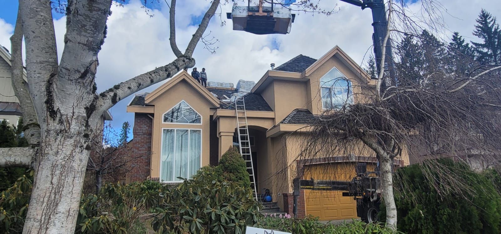 Workers replace the roof of a beige two-story suburban home with a ladder leaning against the front facade.