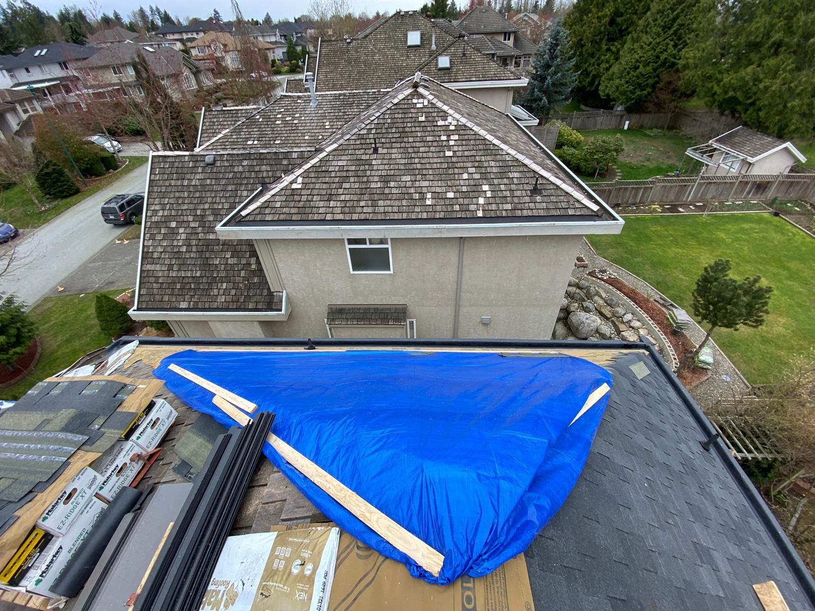 An elevated view of a residential roof under repair, featuring a large blue tarp covering a section of the roofing.