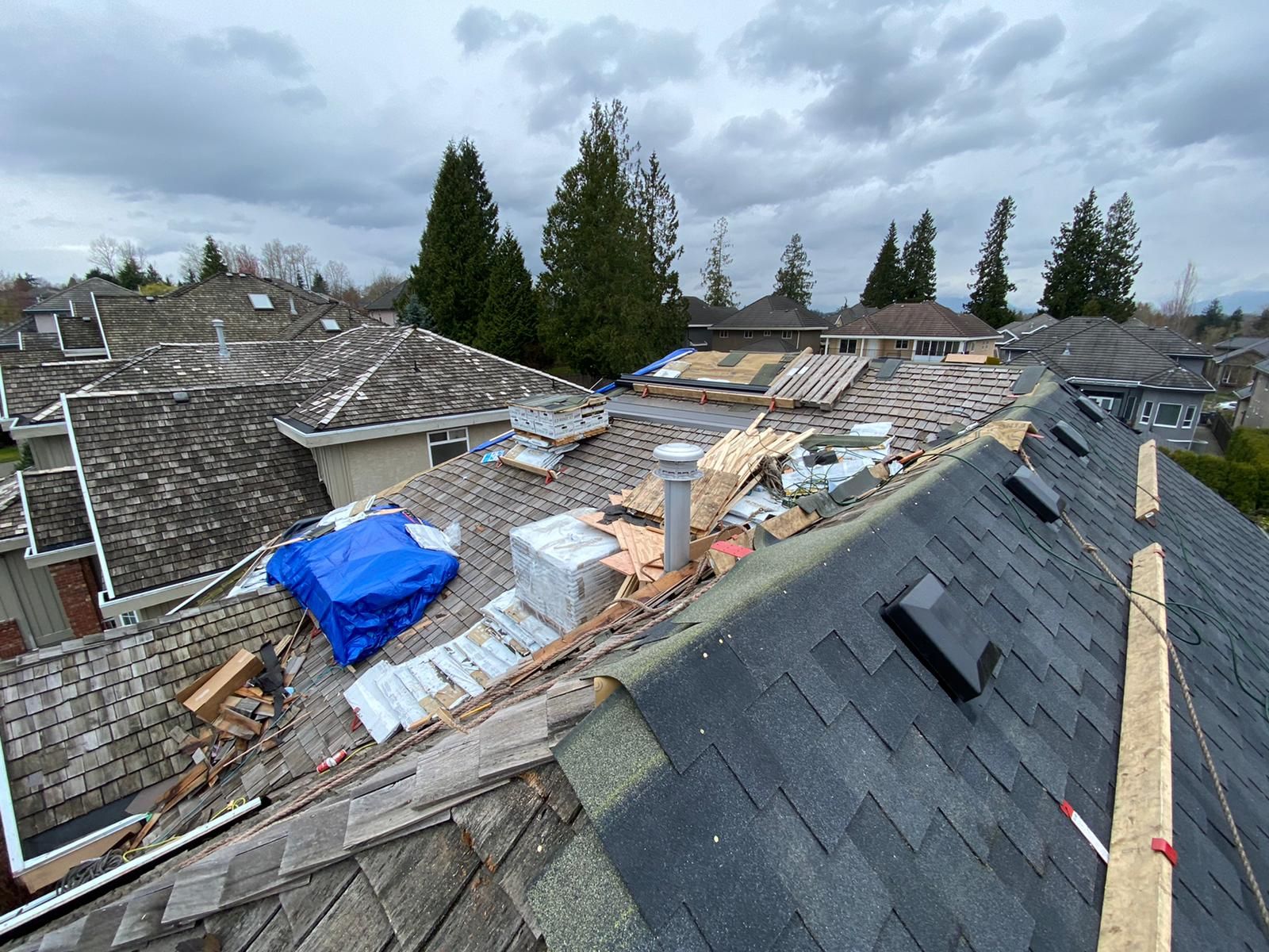 A residential roof undergoing repairs with sections of old shingles removed, exposed wood decking, and a blue tarp.