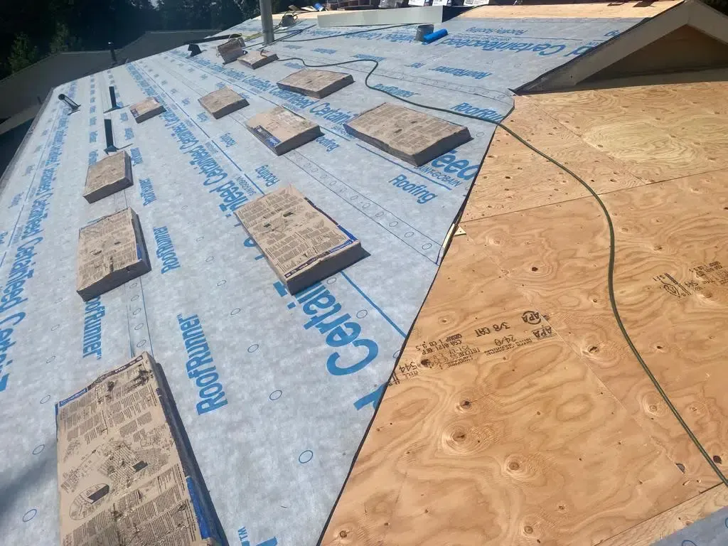 A roof under renovation, with half covered in blue synthetic underlayment and the other half showing exposed plywood.