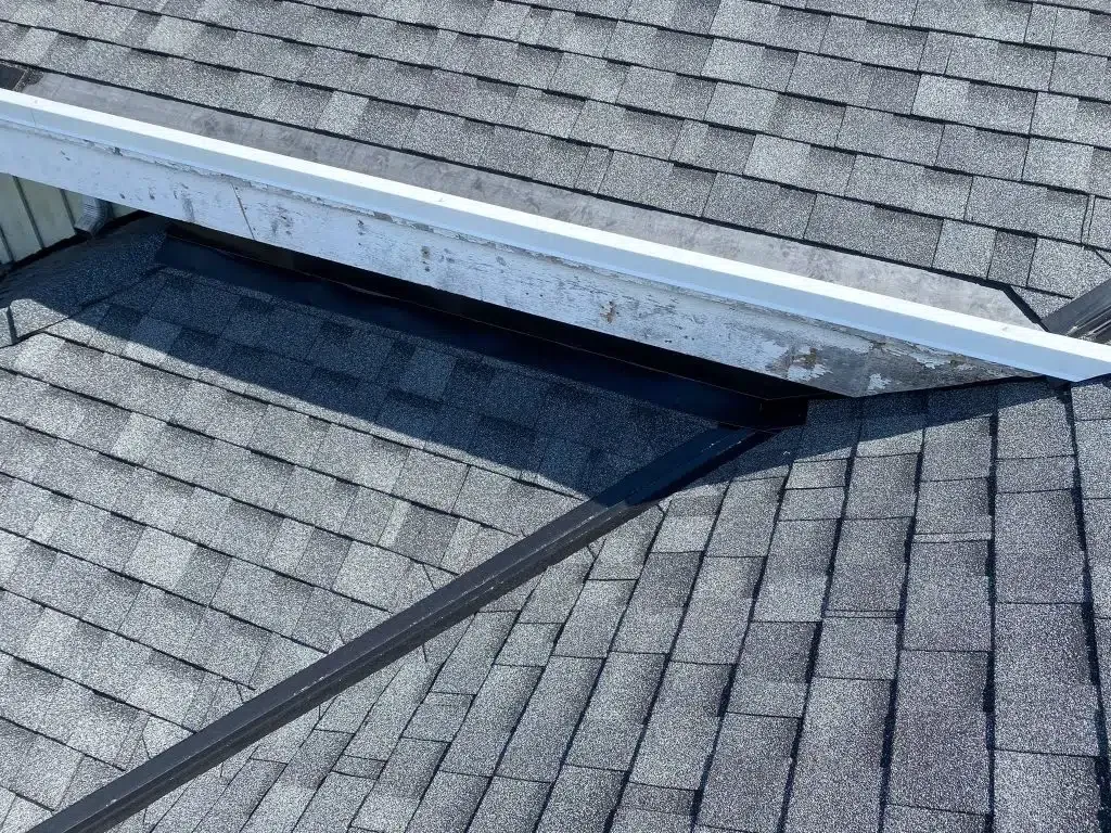 Close-up of a shingled roof intersection with a white metal flashing border and black sealant along the valleys.