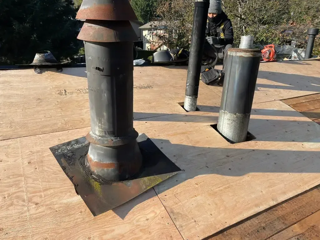 Two black metal rooftop vents on a flat tan roof with pipes and ducting nearby
