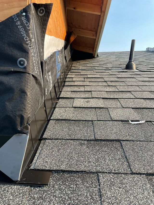 Asphalt shingles beside a wall with exposed underlayment and a roof vent
