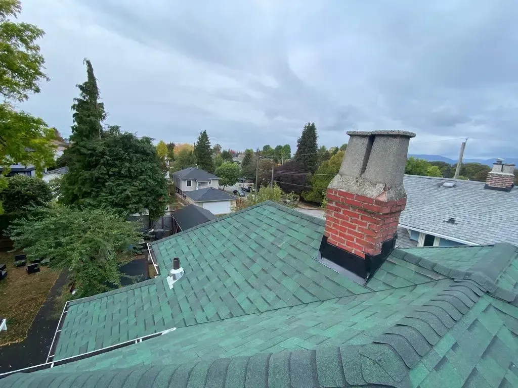 A green roof with a brick chimney on top of it.