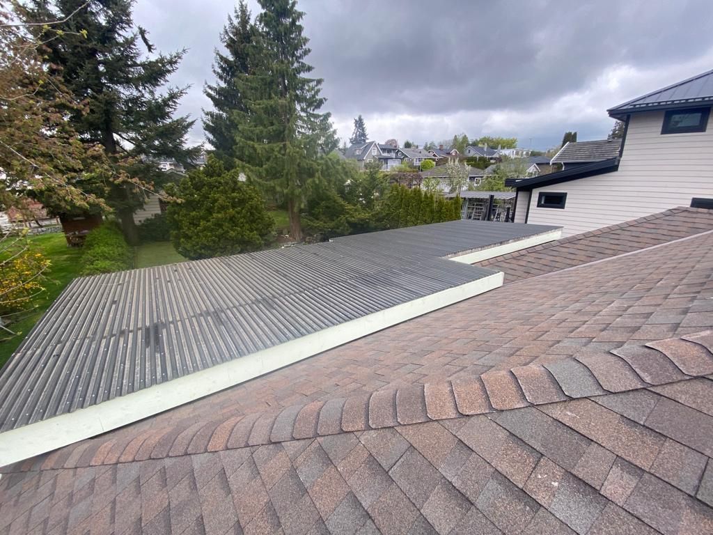 An eye-level view from a roof showing a flat, gray patterned low-slope section adjacent to a brown shingled pitched roof.