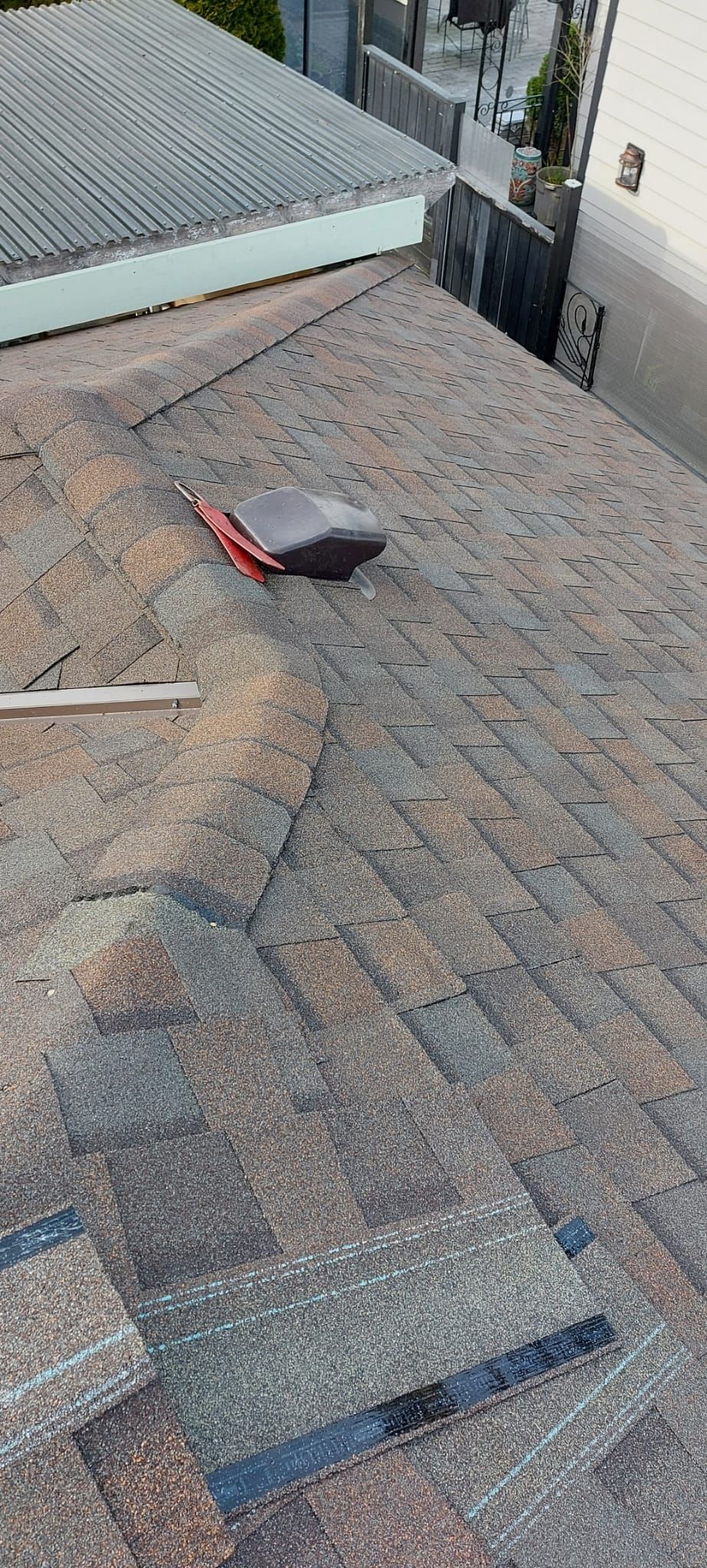 A high-angle view of a residential roof showing damaged shingles and a small, discarded piece of metal roofing material.