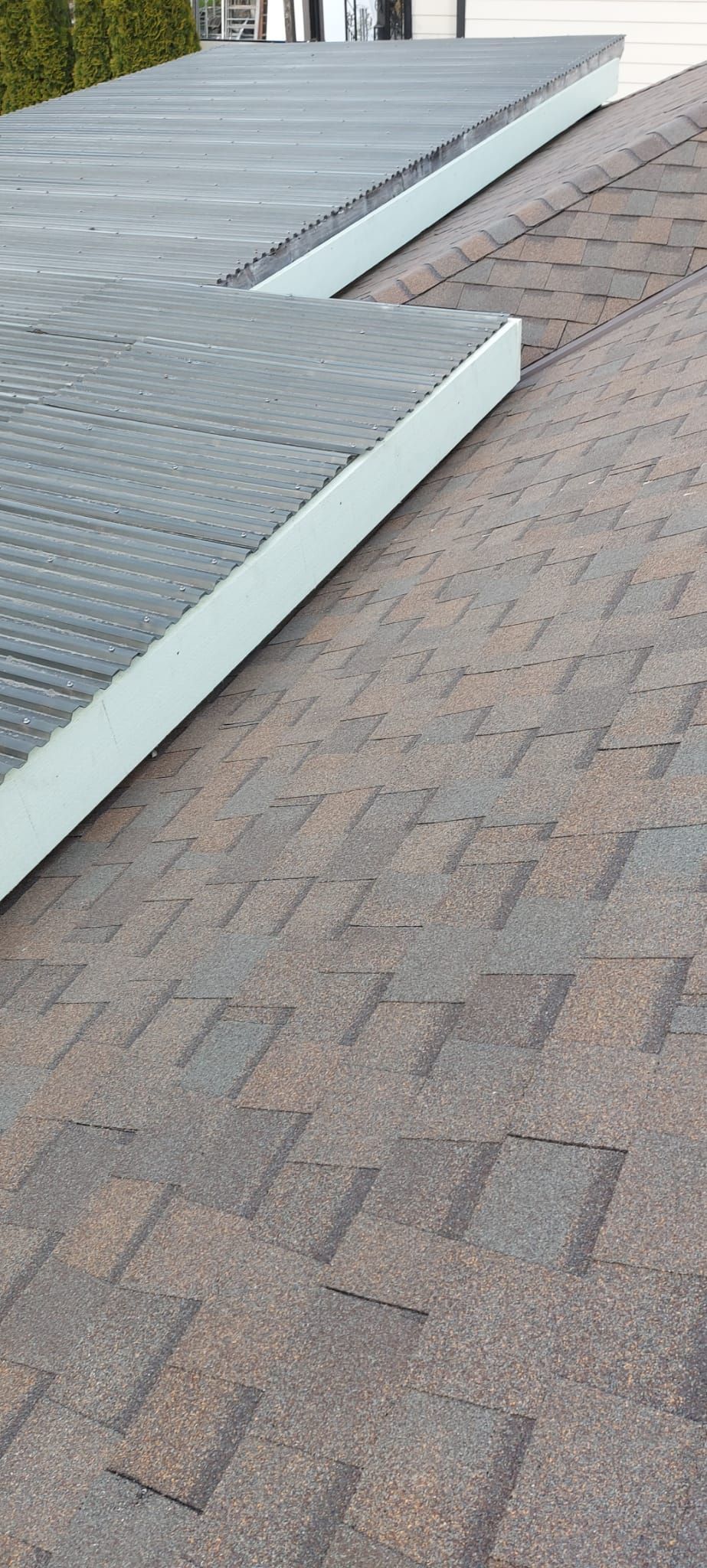 A diagonal view of a brown asphalt shingle roof transitioning to a flat, light-gray surfaced roof section.