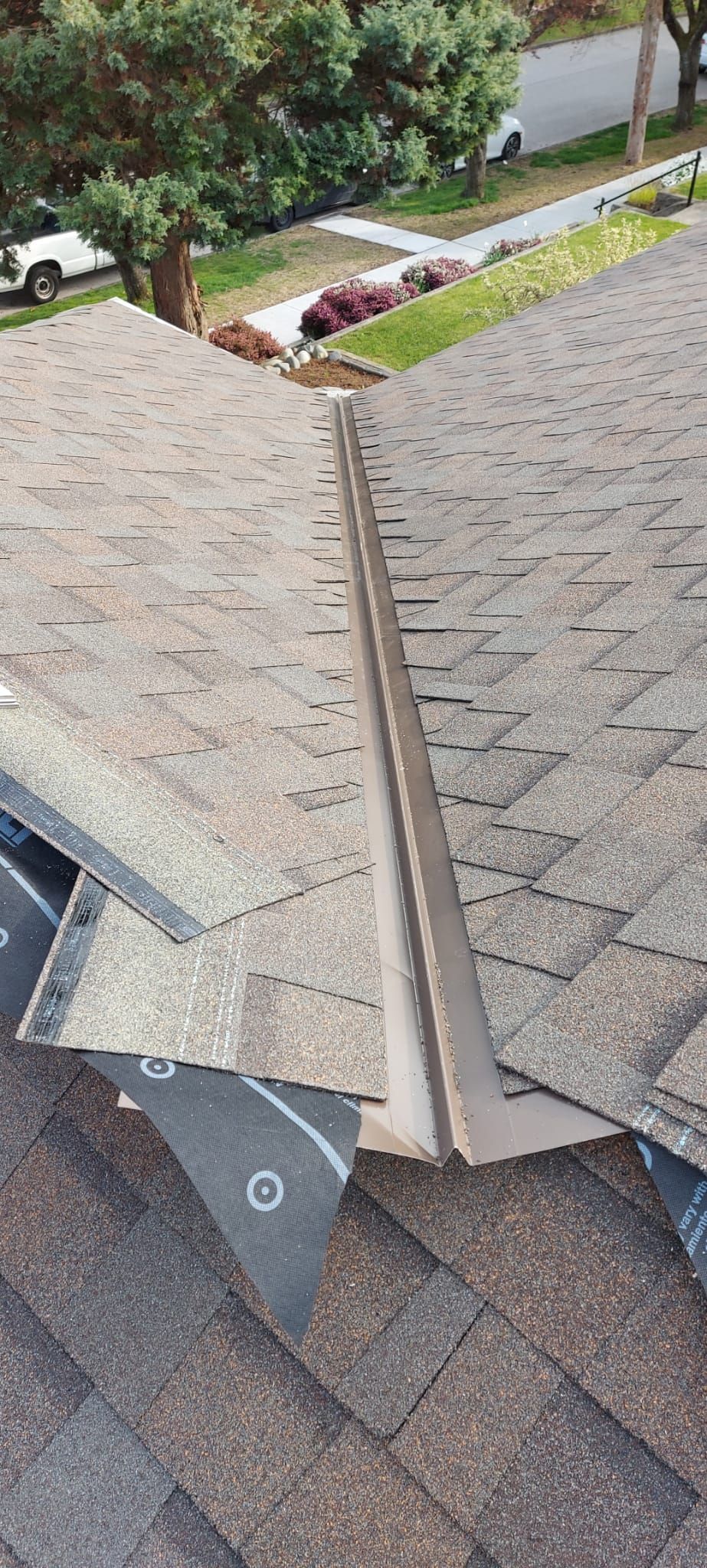 An overhead view of a roof under construction, showing a metal valley transition between two shingled roof sections.
