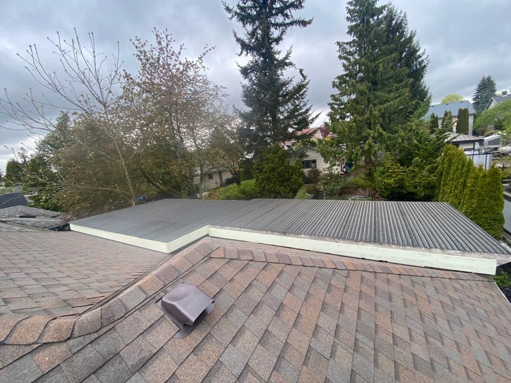 A low-angle view of a residential roof featuring a flat, gray, layered section transitioning to shingled, sloped roofing.