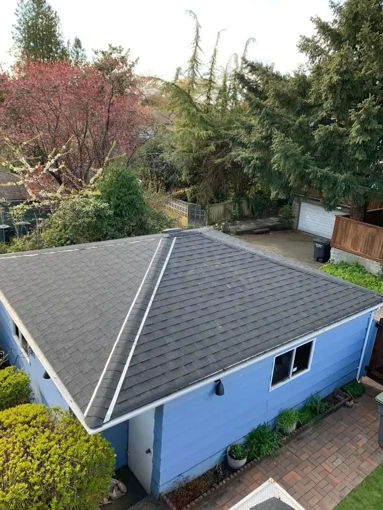 An overhead view of a light blue detached garage with a dark gray shingled roof, surrounded by trees and a brick walkway.