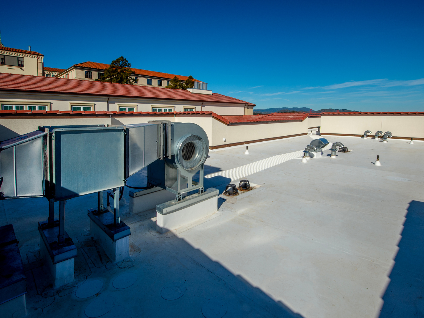Large industrial HVAC equipment sits on a flat, light-colored building rooftop under a clear blue sky.