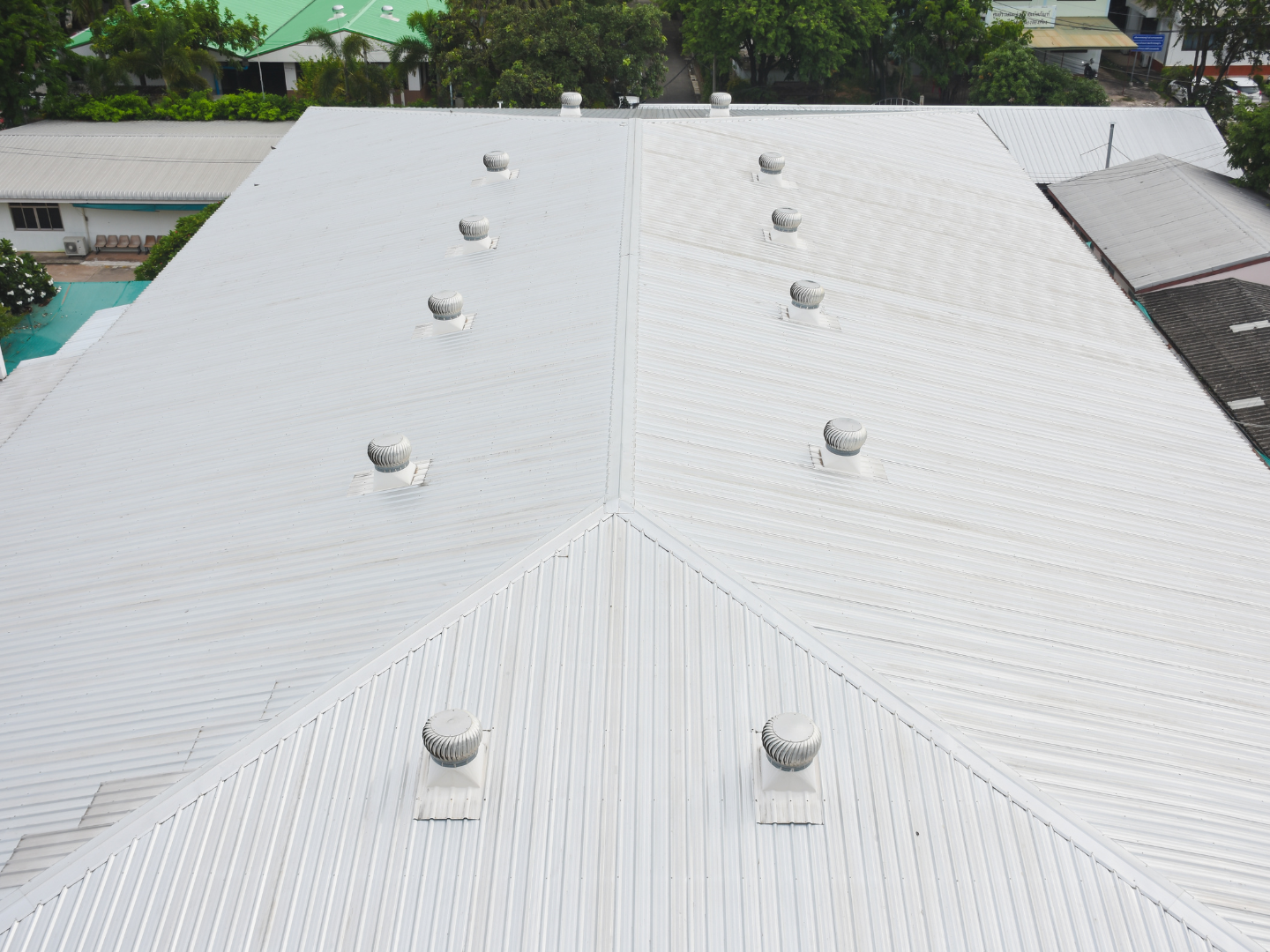 An elevated view of a white, gabled metal roof with several round, silver turbine ventilators installed in rows.