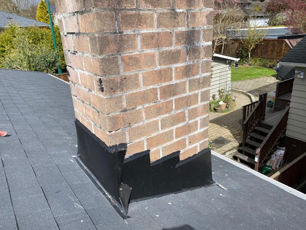 A brick chimney is sitting on top of a black roof.