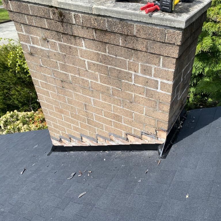A brick chimney is sitting on top of a black roof with new cricket installed