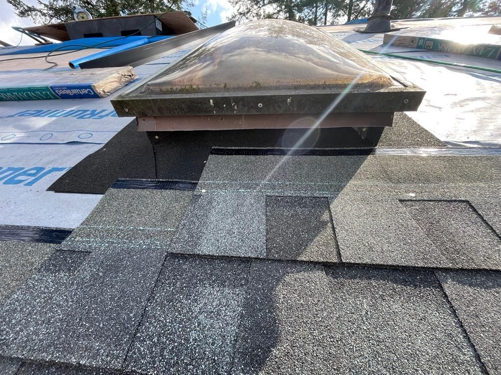 A view of a rectangular skylight installed on a residential roof being covered with gray asphalt shingles.