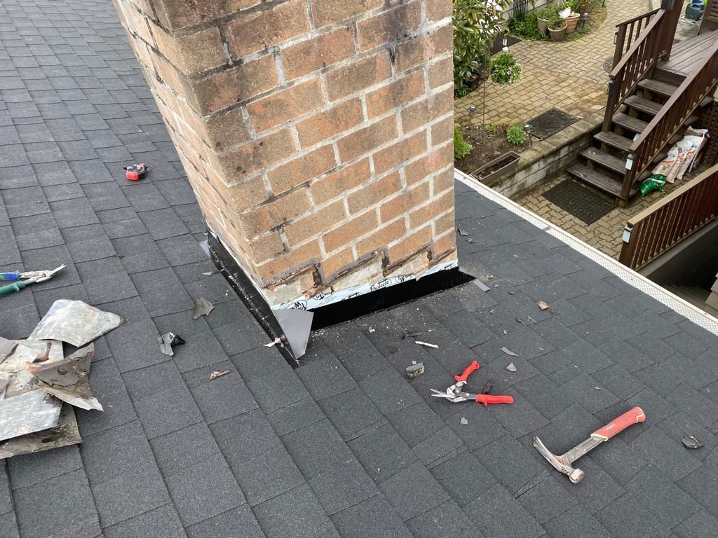 A brick chimney is sitting on top of a roof next to a hammer and pliers.