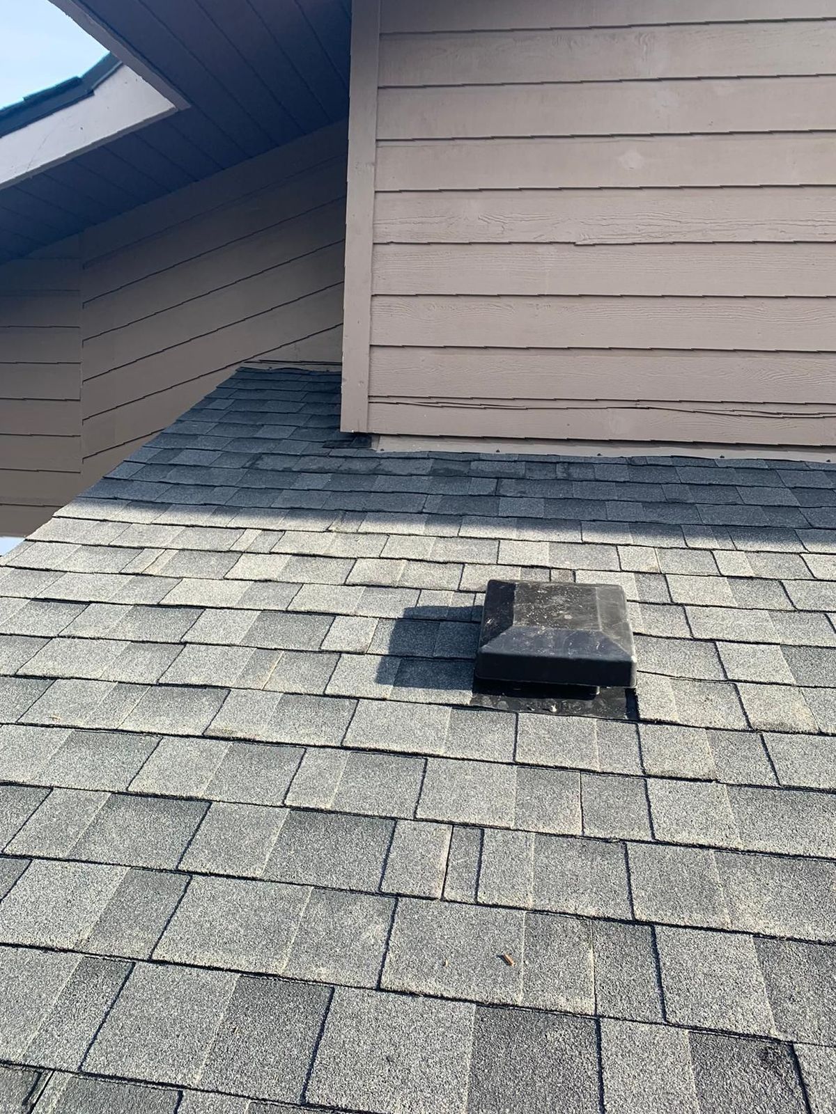 A roof with a vent on it and a building in the background.