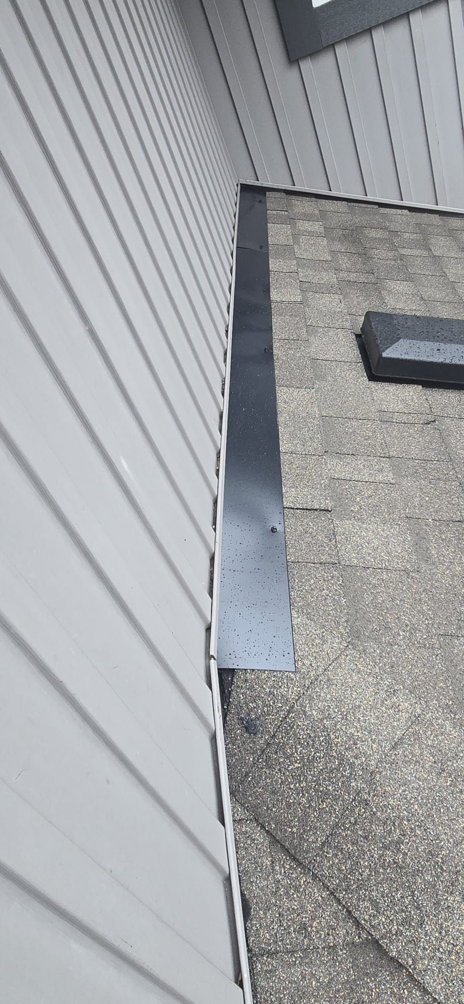Black metal roof to wall flashing along grey siding with a box vent on the shingles, 229 St Maple Ridge BC, Paragon Roofing BC