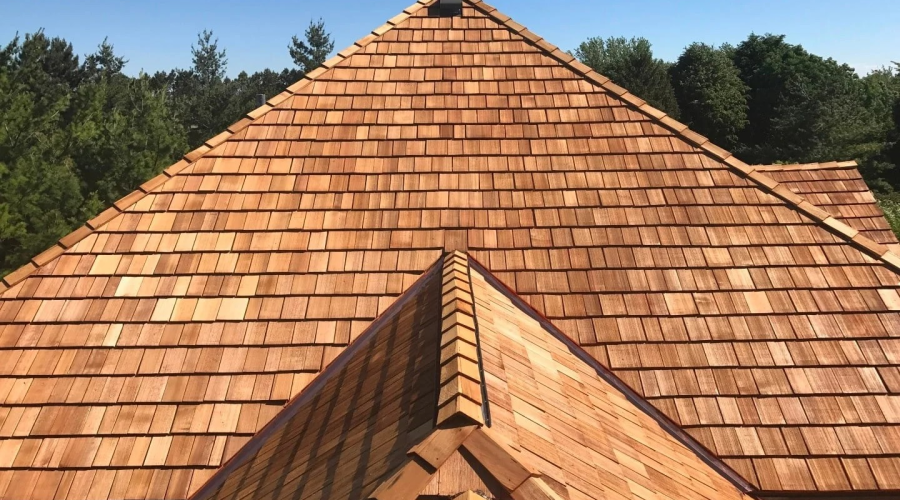 A high-angle view of a newly installed wooden shingle roof with a hip-roof design and dark metal edging.