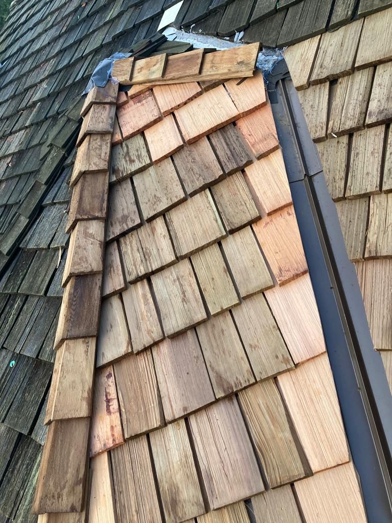 A roof with a vent on it and a building in the background.