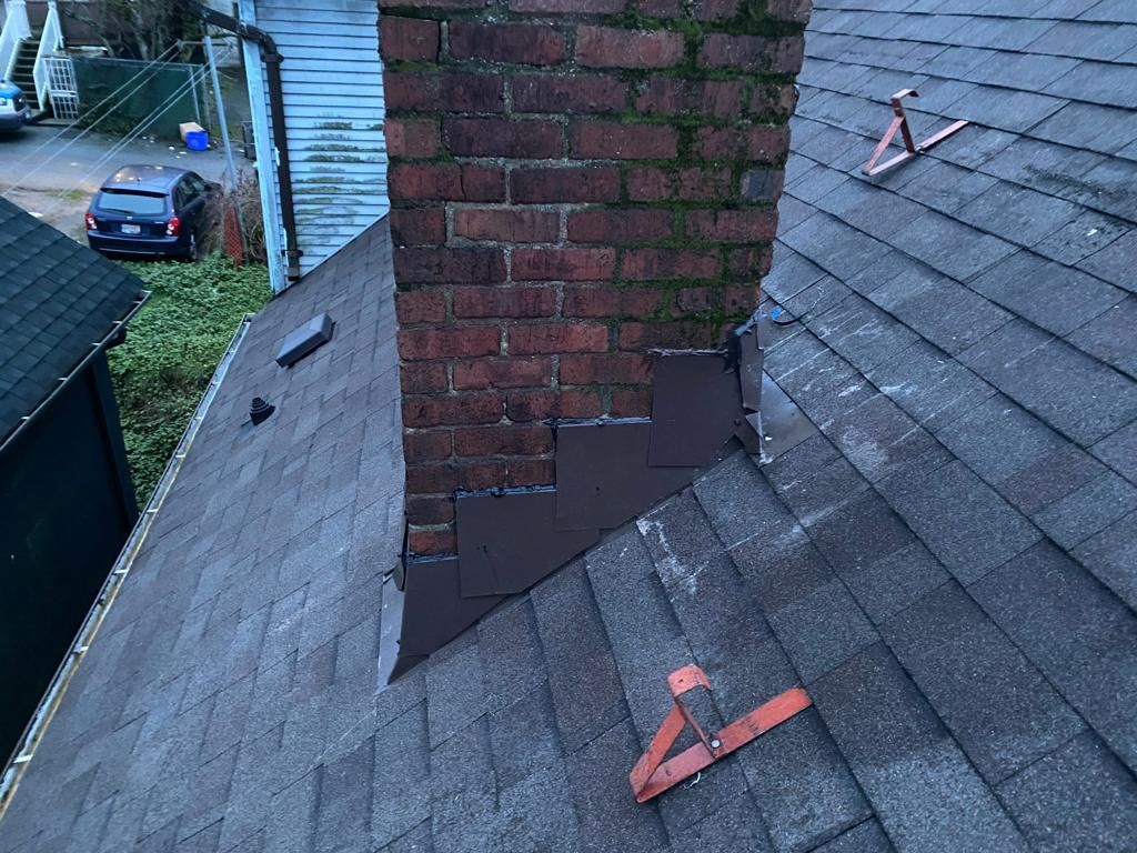 A roof with a vent on it and a building in the background.