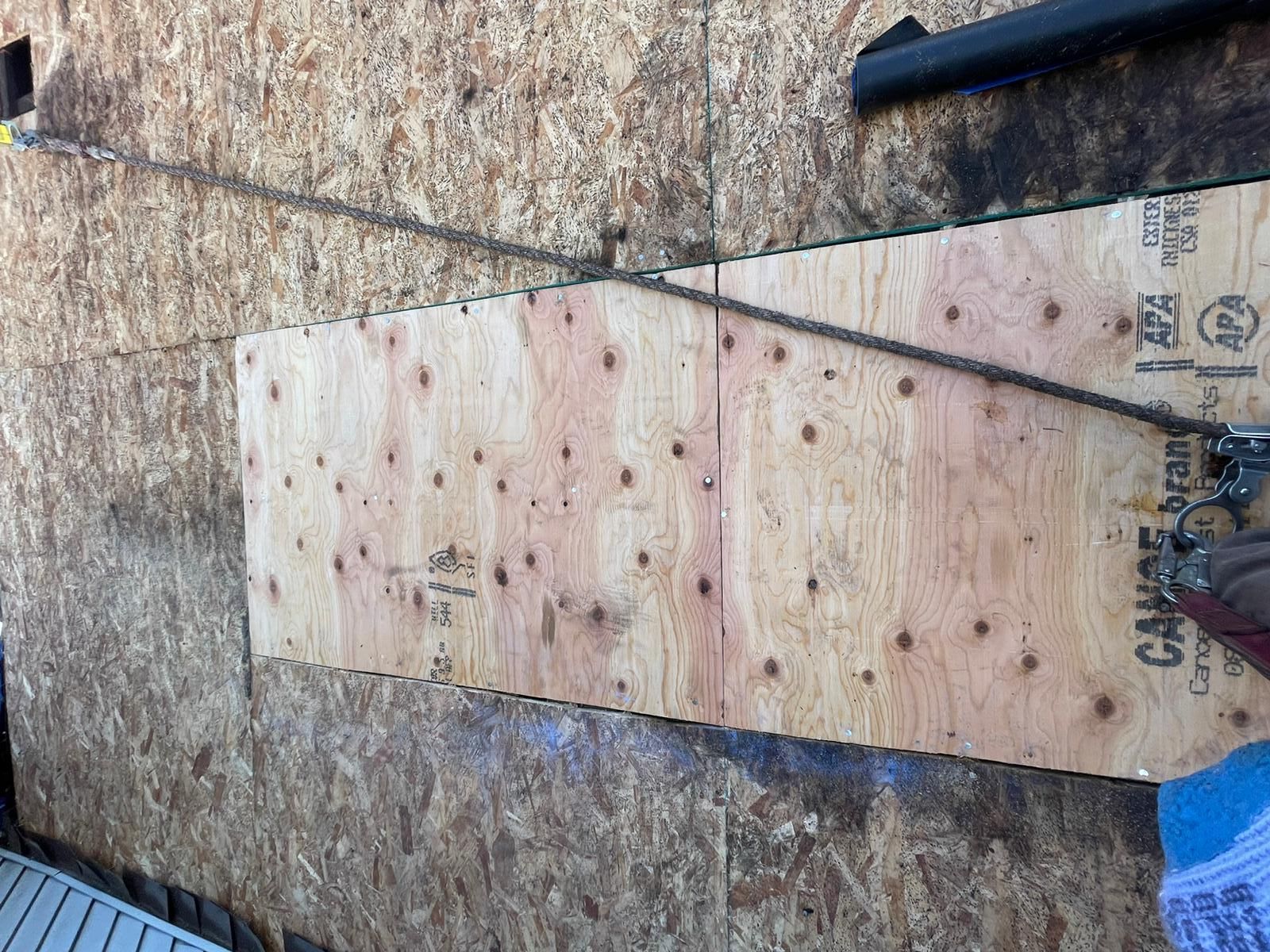 A person is cutting a piece of plywood on a wall.