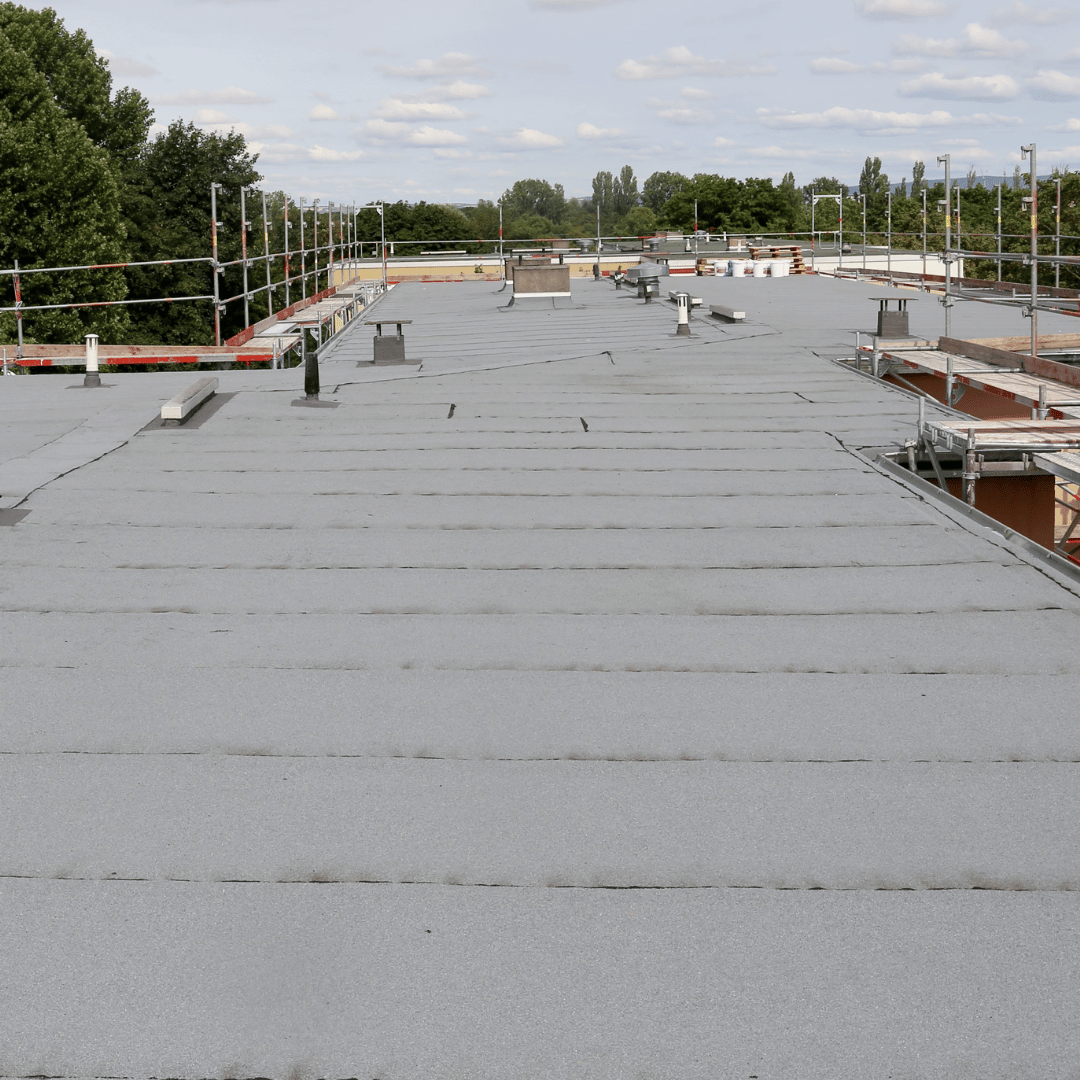 Flat, gray roof with vents and scaffolding under a cloudy sky.