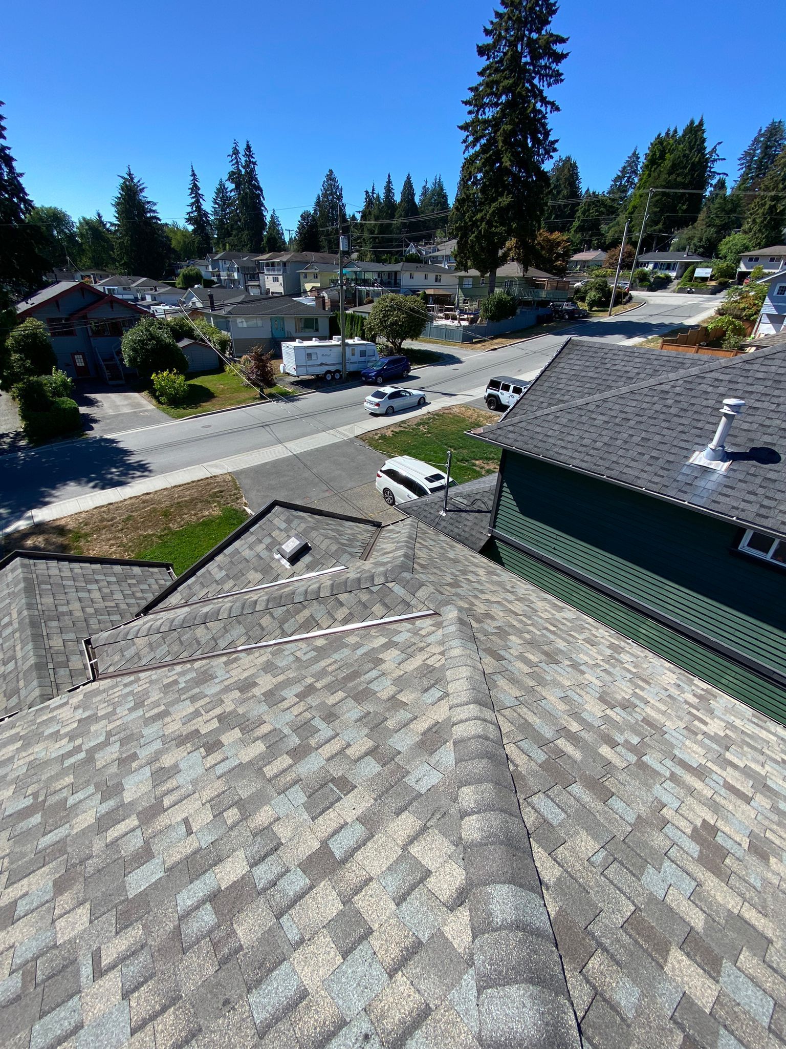 An elevated, high-angle view looking down at residential gray shingle roofs, neighborhood streets, and trees under a sky.