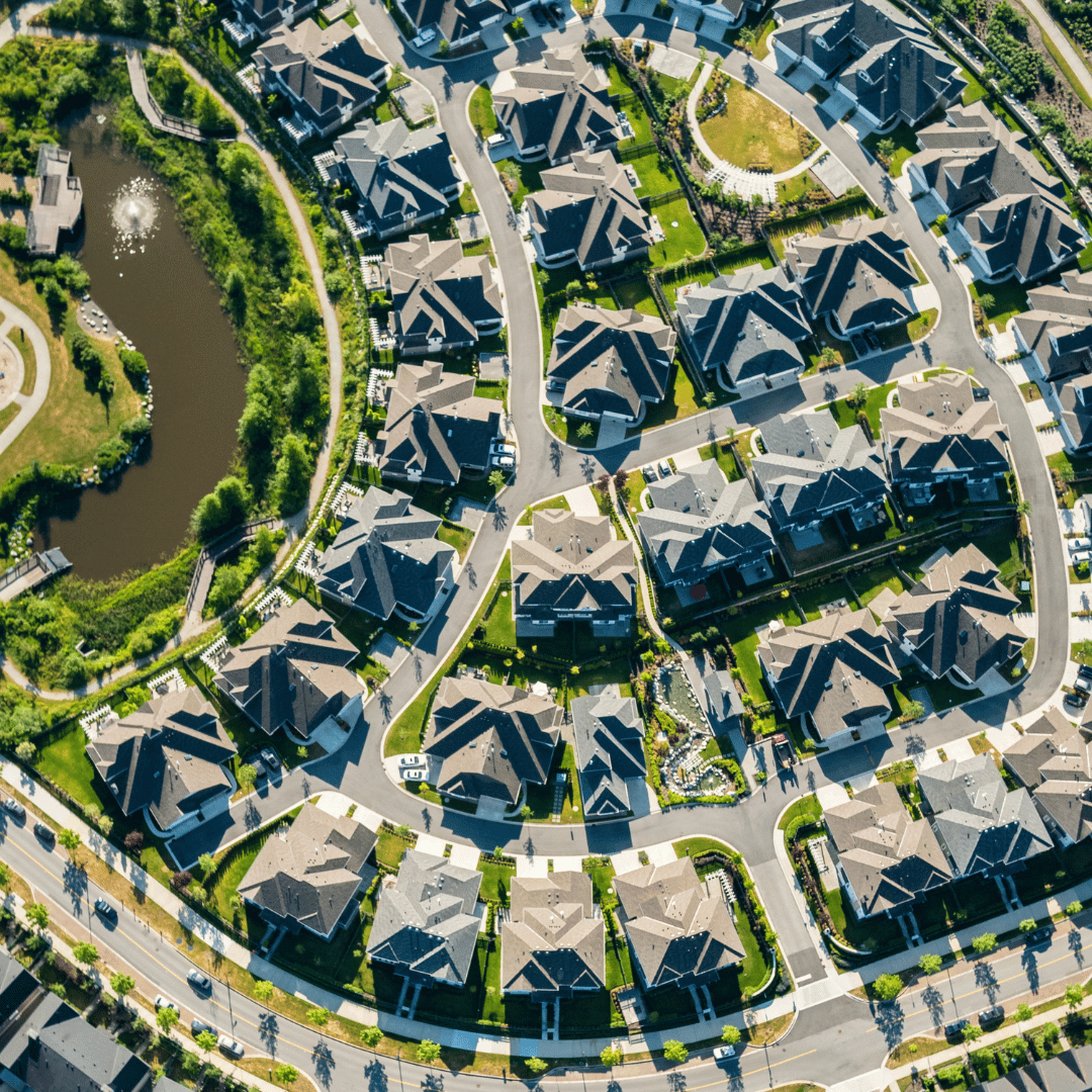 Aerial view of a suburban neighborhood with houses, winding streets, and a pond surrounded by greenery.