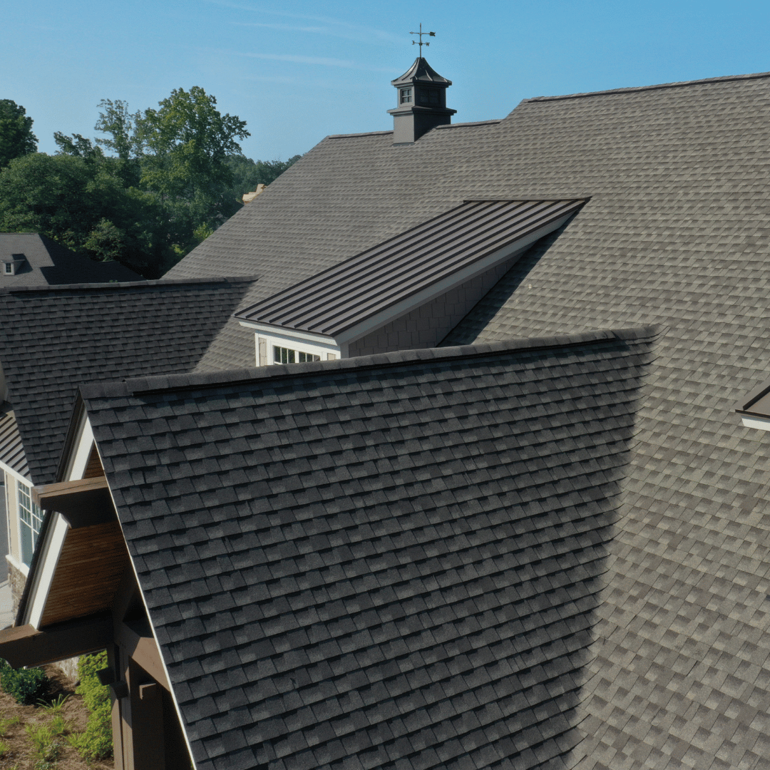 Aerial view of a residential shingle roof with a central metal-roofed dormer and a rooftop cupola.