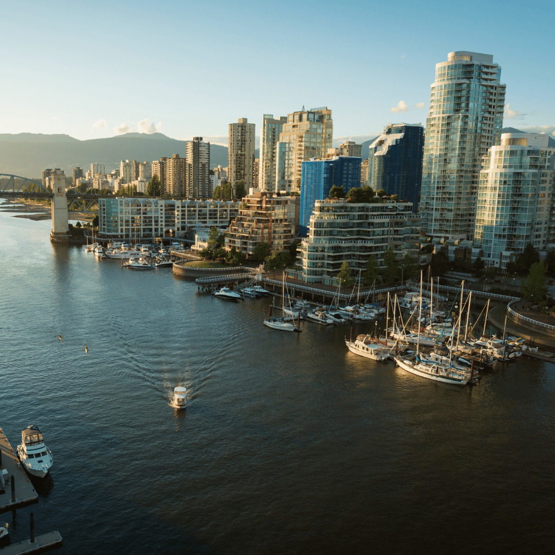 A waterfront cityscape with high-rise buildings, a harbor full of moored boats, and mountains in the distance.