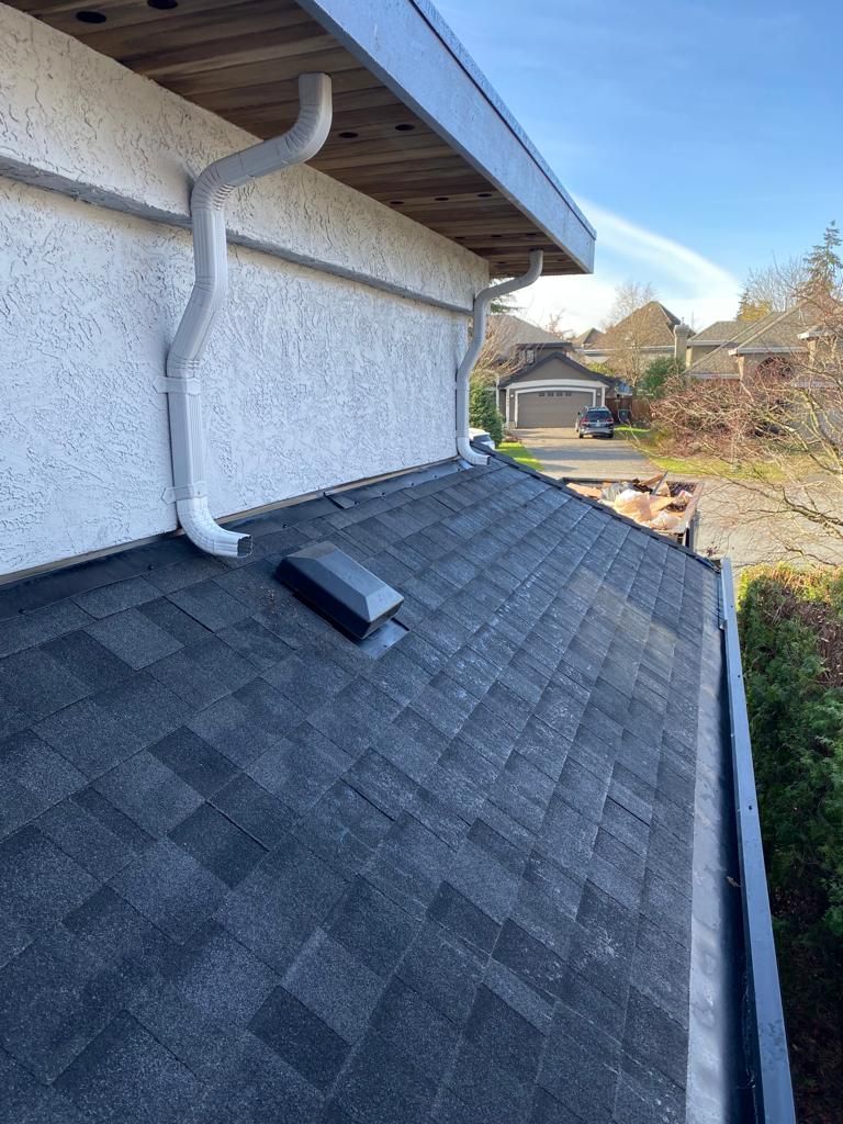 A slanted asphalt shingle roof with a square vent, featuring a white gutter system mounted along the adjacent stucco wall.