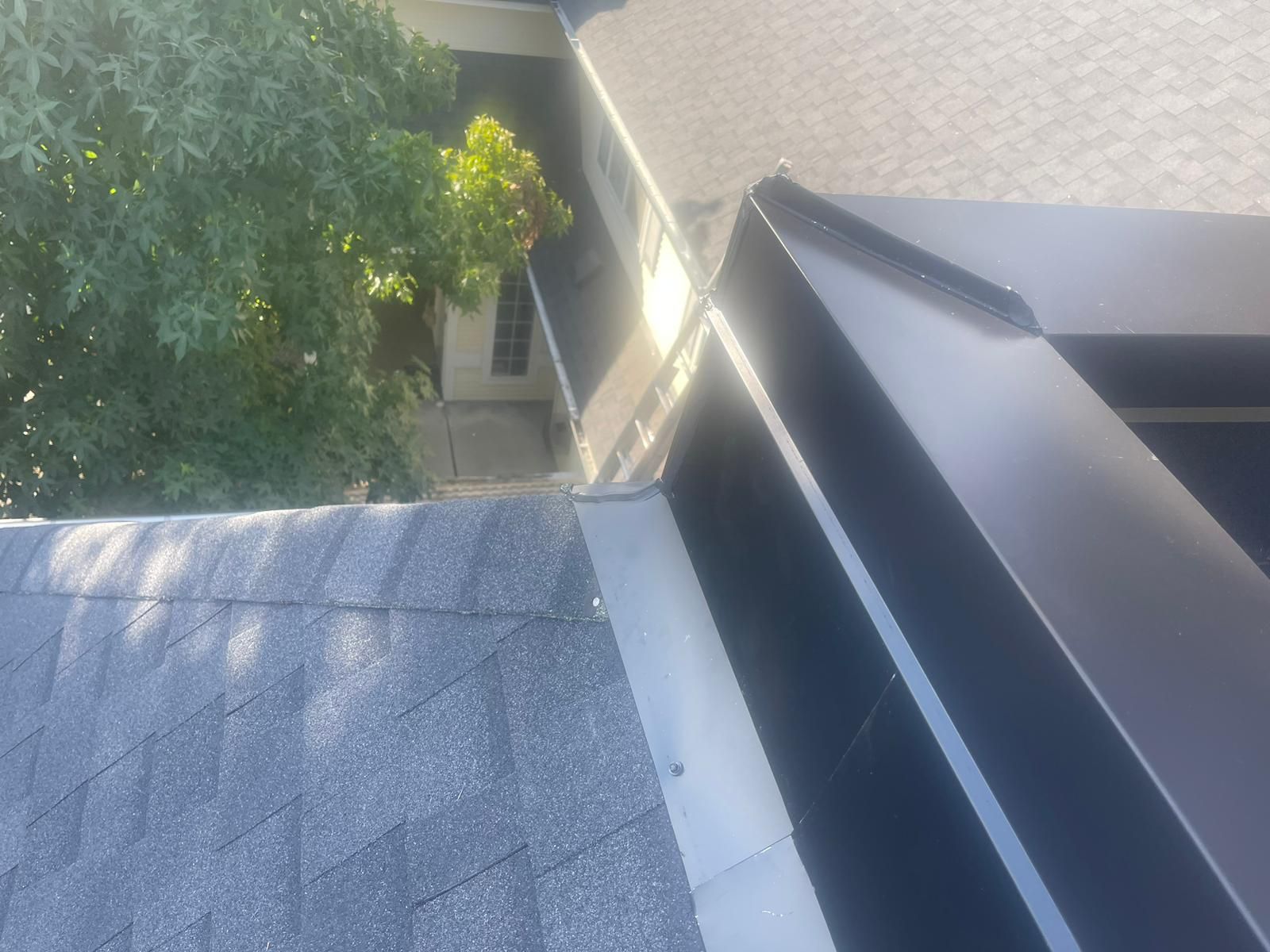 A close-up view of a shingled roof transitioning to metal flashing and a dark brown metal roof edge.