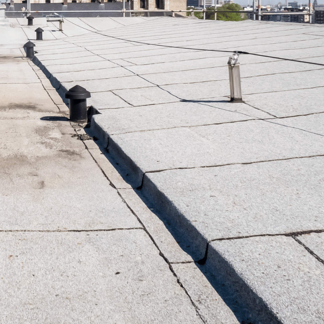 A gray, flat commercial roof featuring multiple ventilation pipes and a raised seam divider in the foreground.