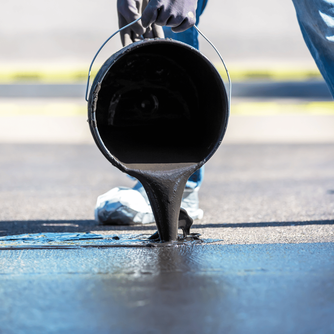 Worker pouring black asphalt from a bucket onto a road surface