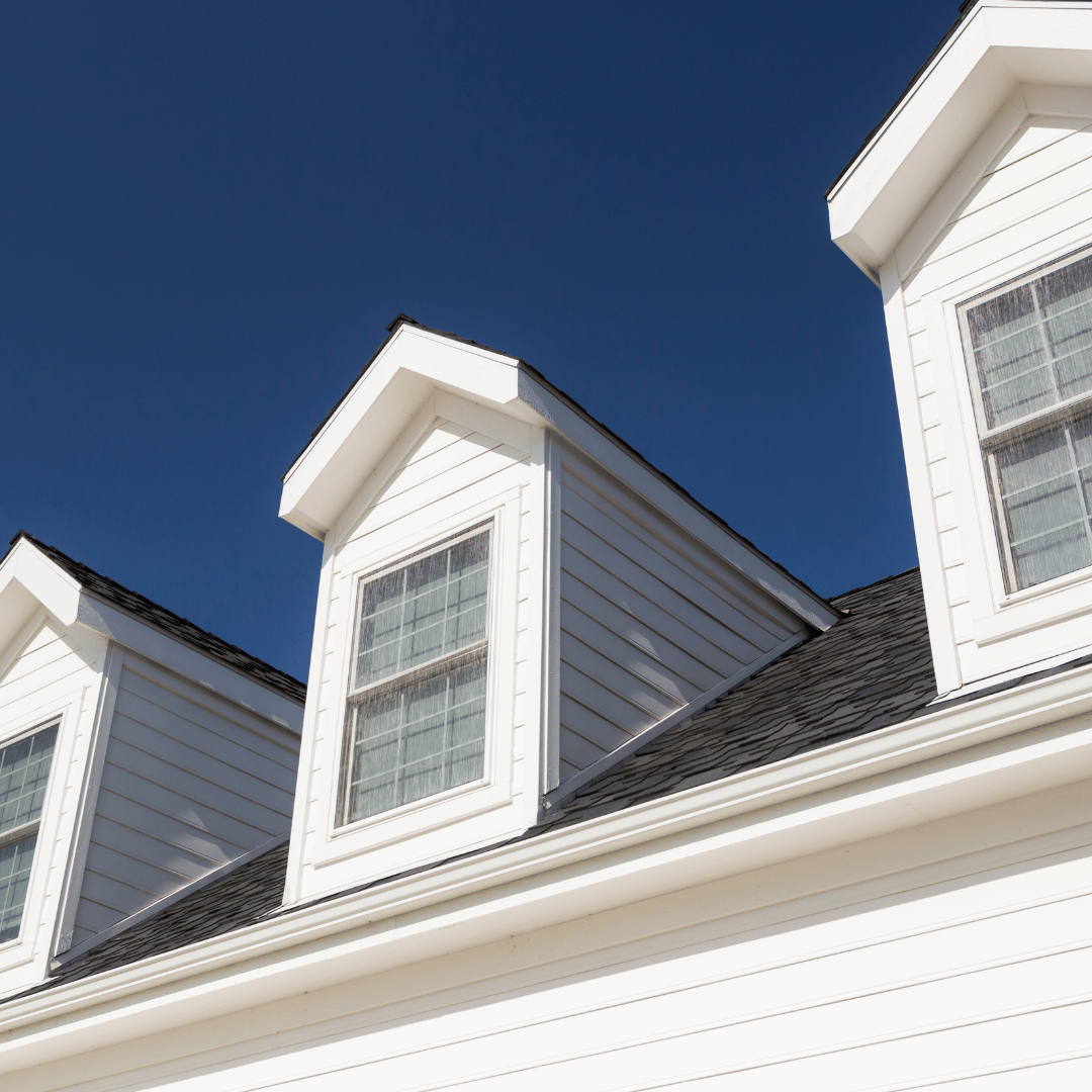 White exterior siding and multiple dormer windows on a house with a shingled roof against a clear, deep blue sky.