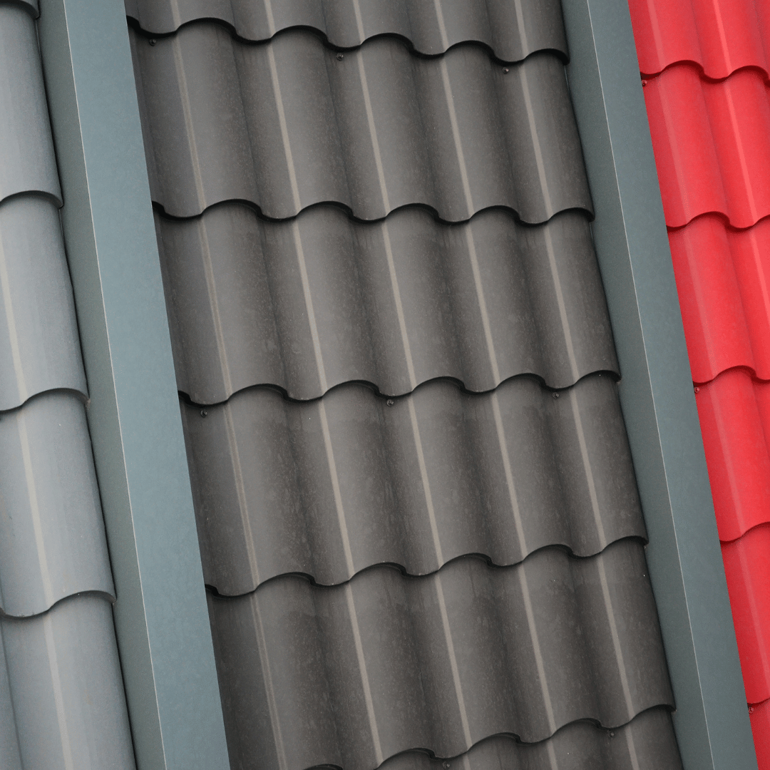 Three samples of corrugated metal roofing tiles in light gray, dark charcoal, and bright red.