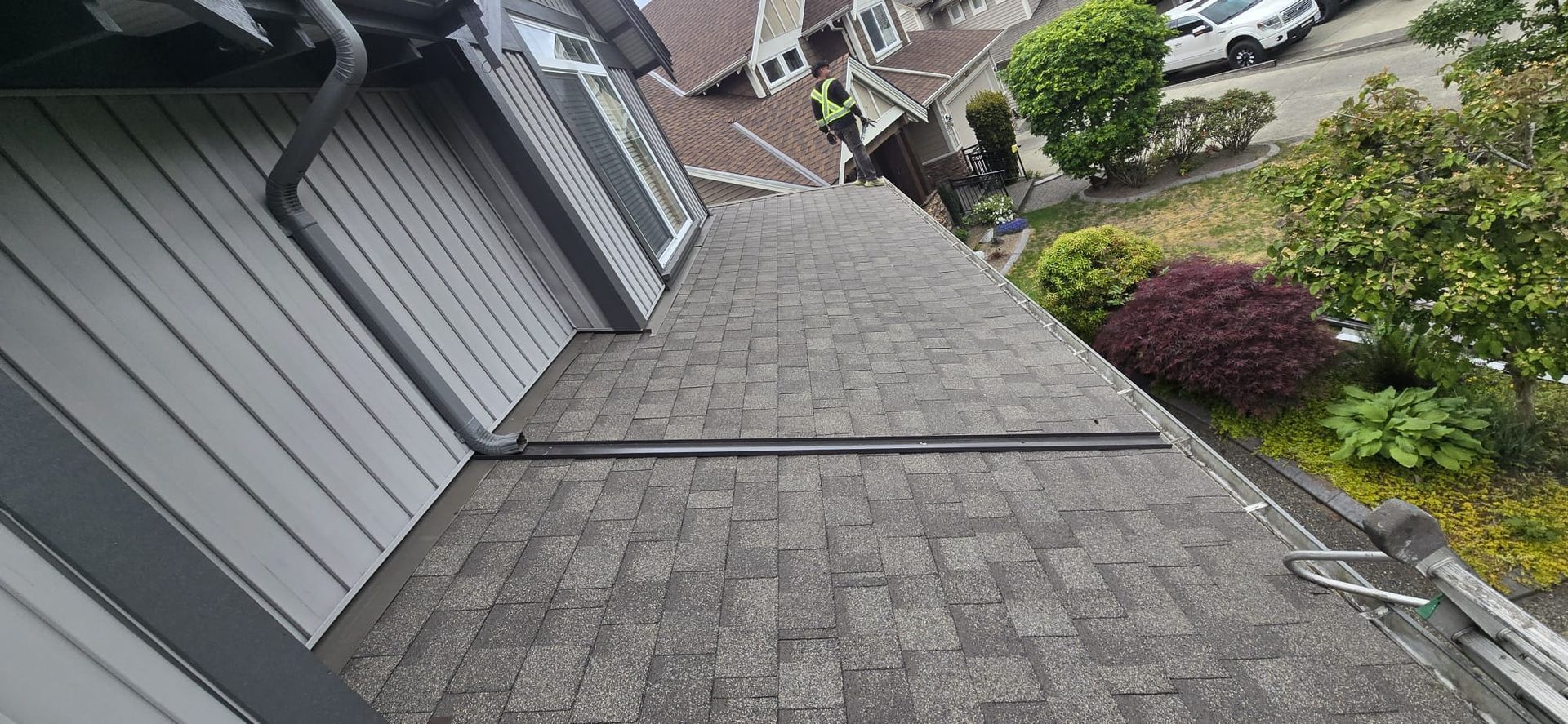 Upper downspout discharging onto a finished lower roof plane with a black diverter and a Paragon crew member on the roof, 229 St Maple Ridge BC