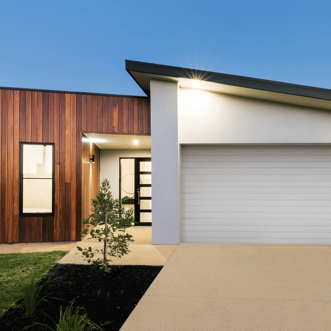 A modern house exterior at dusk featuring wood-paneled walls, a white garage door, and a glass-paneled front door.