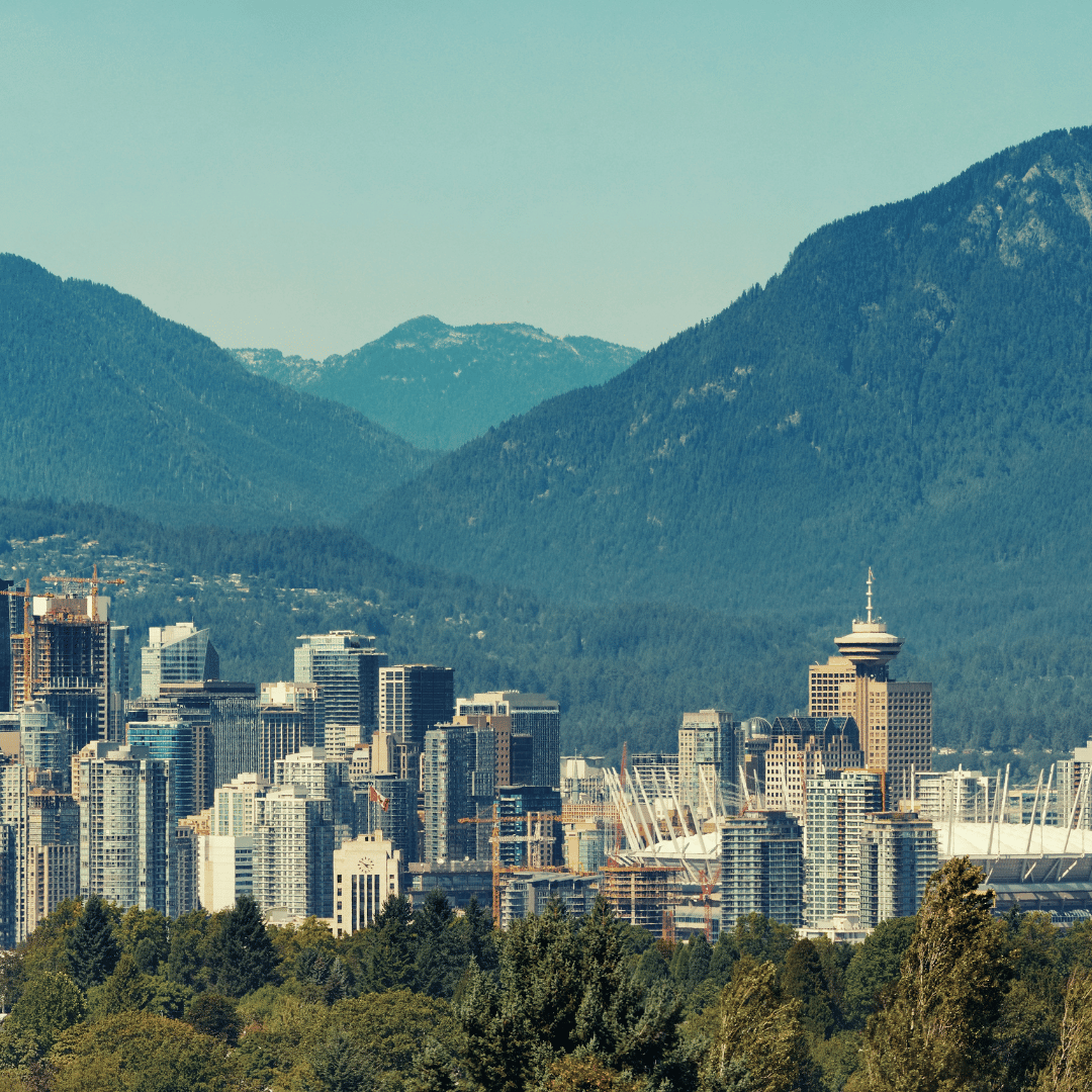The Vancouver skyline features tall city buildings nestled against a backdrop of prominent, blue-toned mountains.