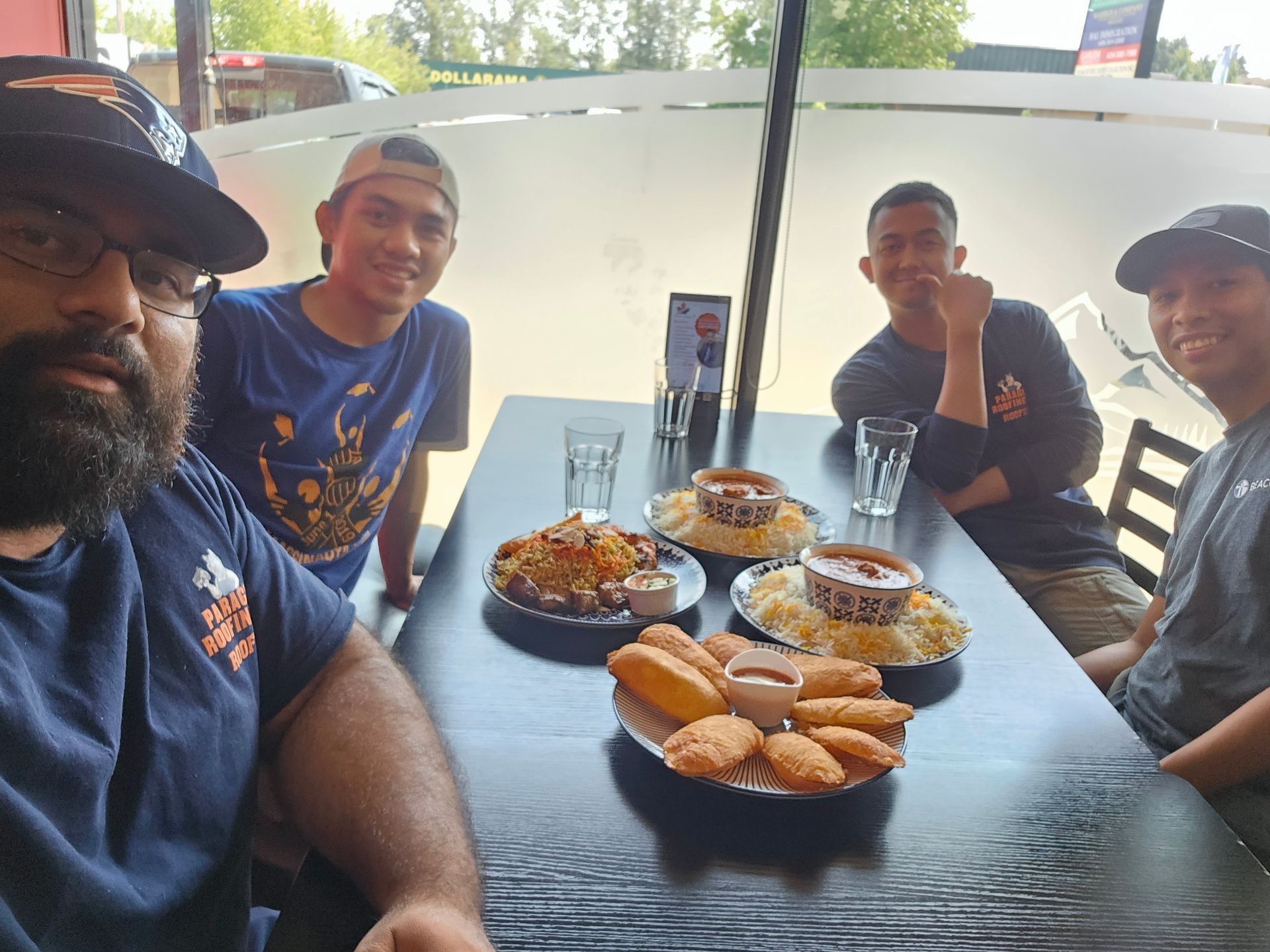 Four friends smile while dining at a restaurant, with plates of food and drinks arranged on a table between them.