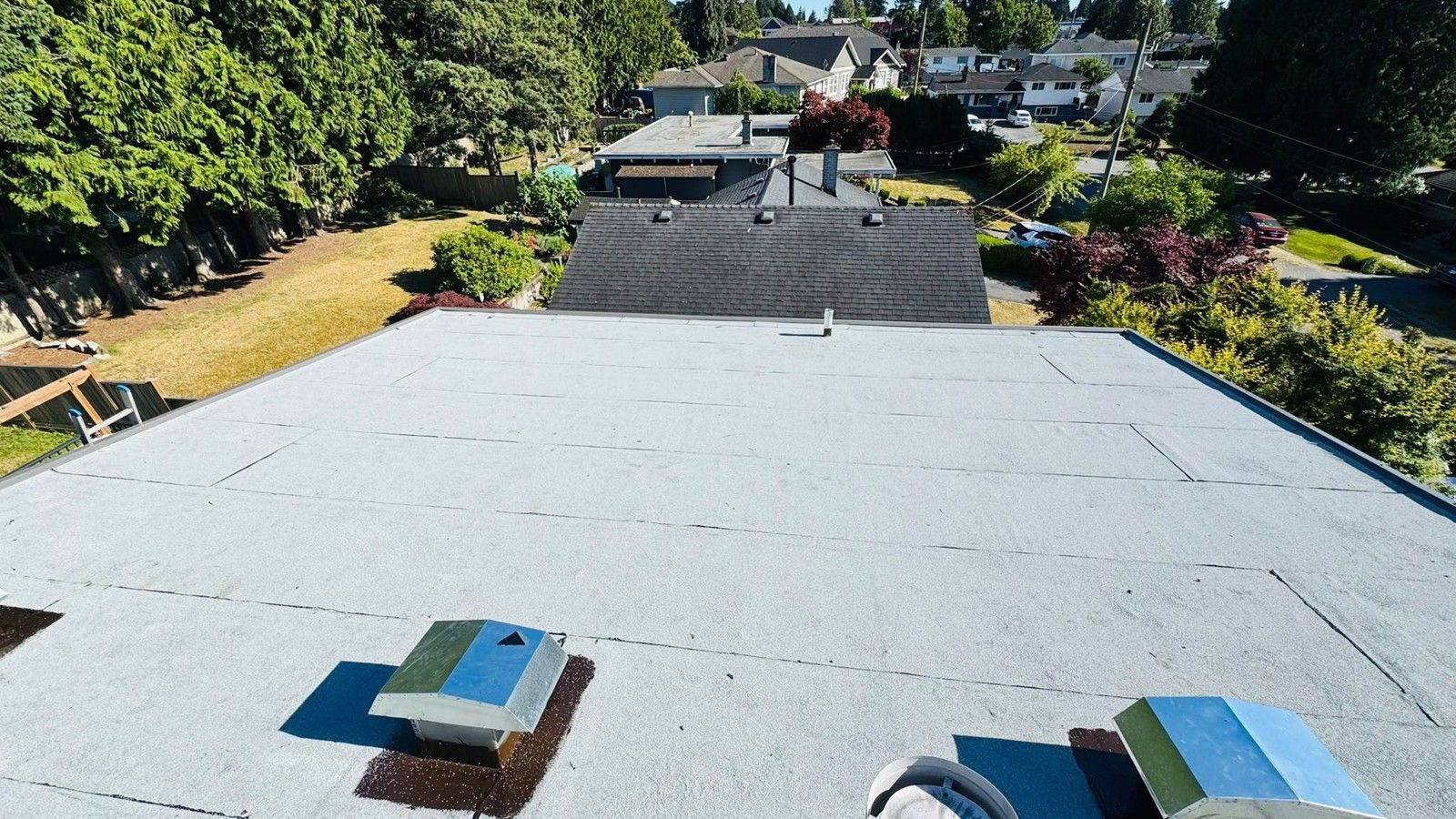 Grey granule surfaced roof with membrane laps, metal vents and houses beyond