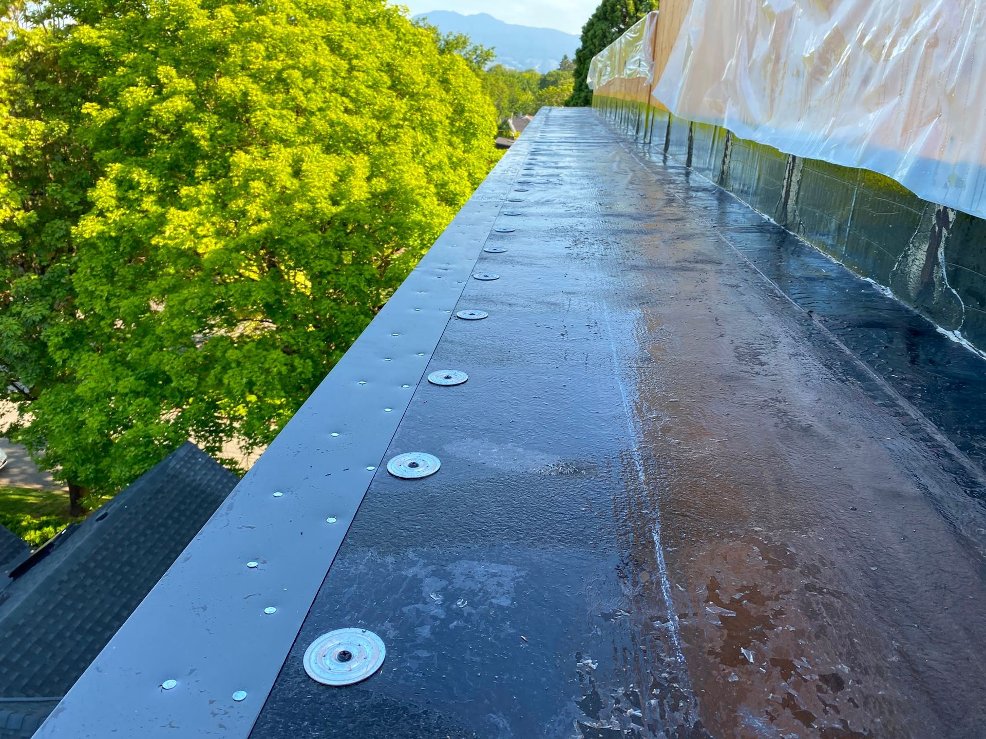 Roof perimeter during preparation, with metal edging, round fastening plates and membrane turning up a wall.