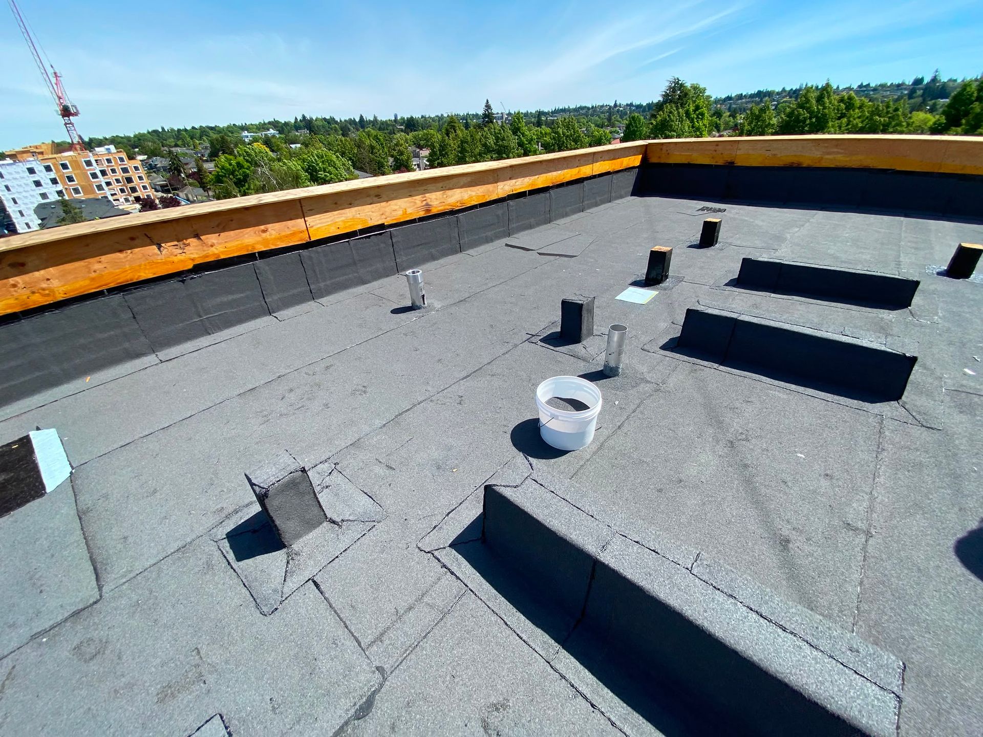 Granular membrane roof around raised curbs and pipe penetrations, with unfinished parapet tops.